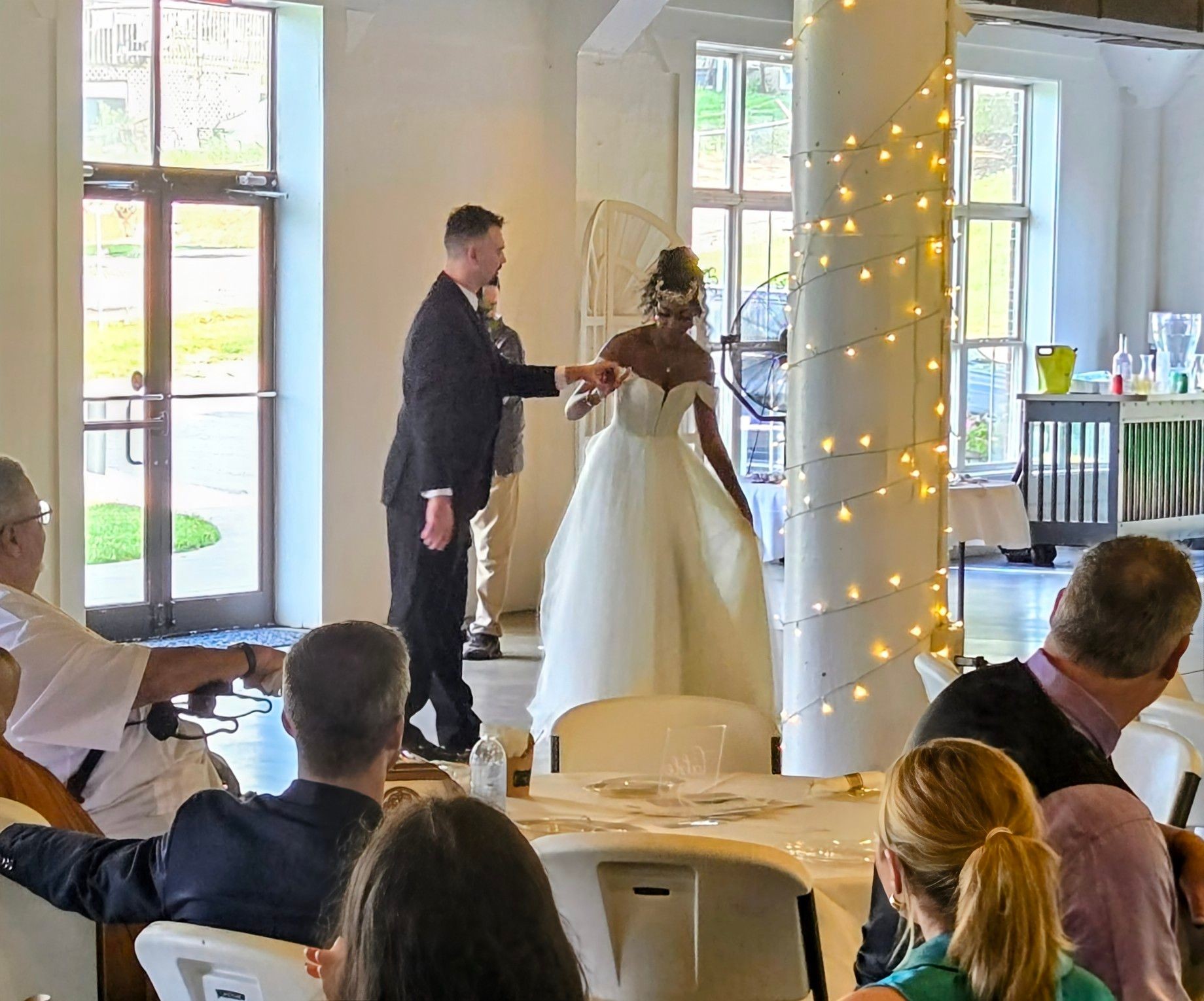 Bride and groom dancing at reception with guests watching, decorated pillar with lights in the foreground.