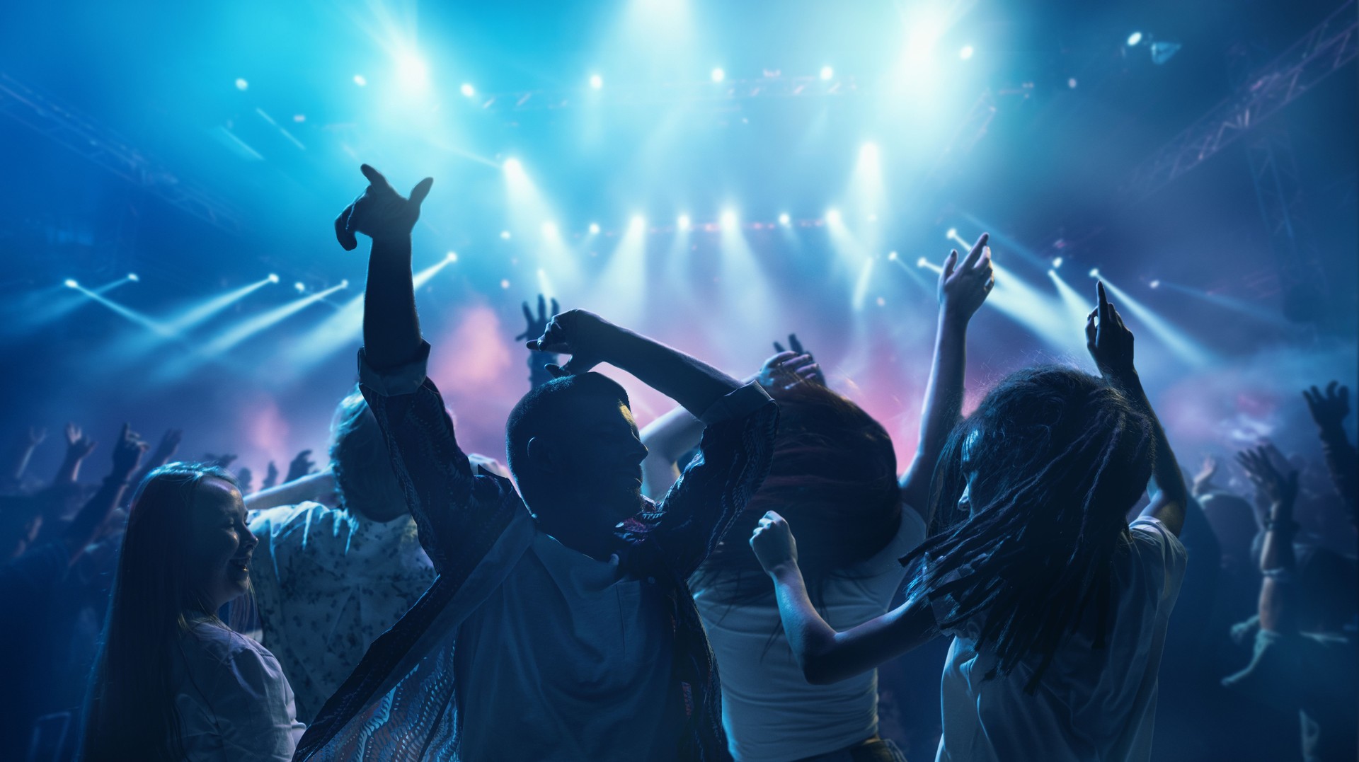 Happy, overjoyed people, students dancing raising hand and singing in neon light, spotlights indoor on party.